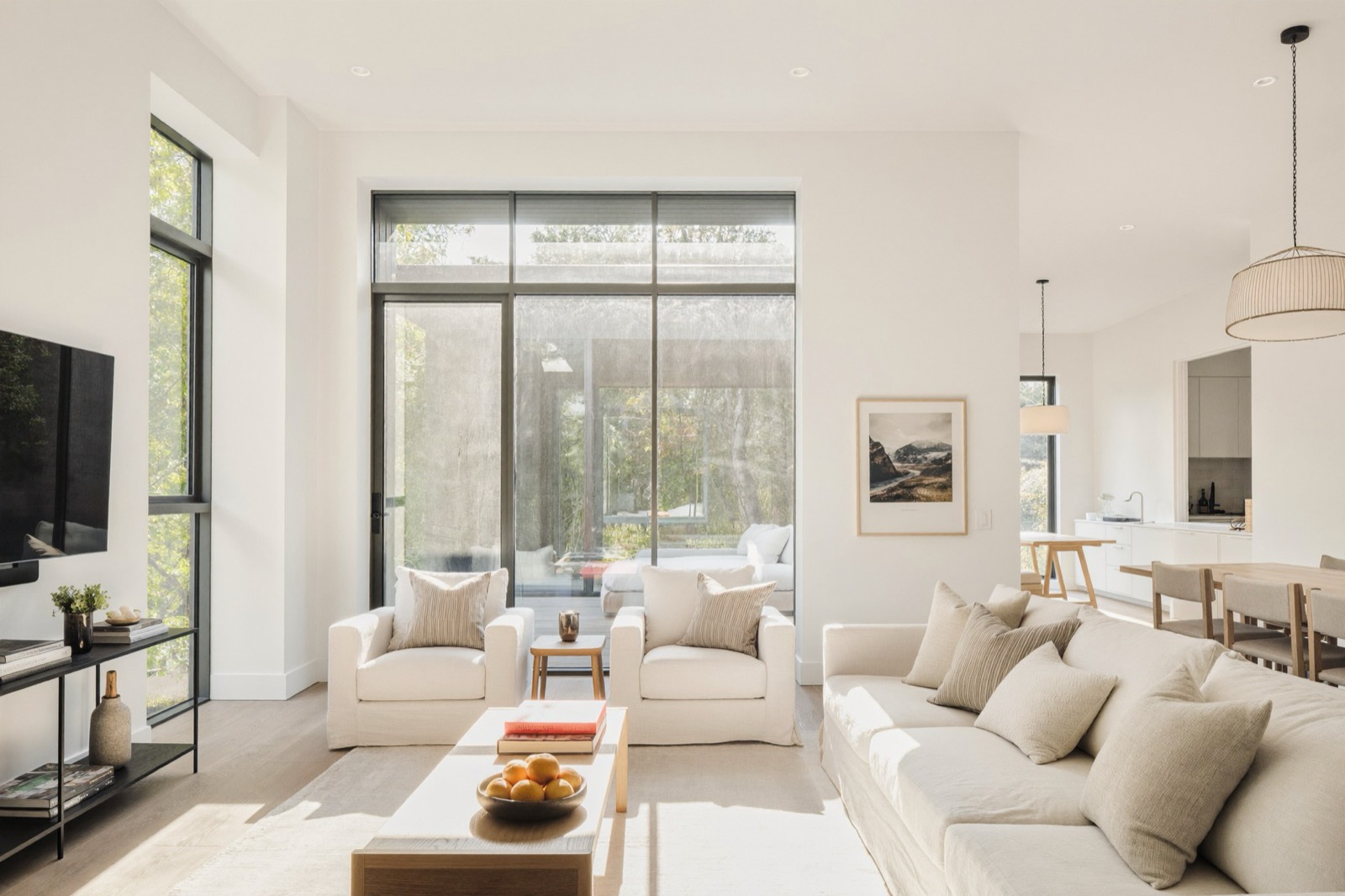 A living room with pale linen sofas, full-height glass onto a deck and trees beyond.